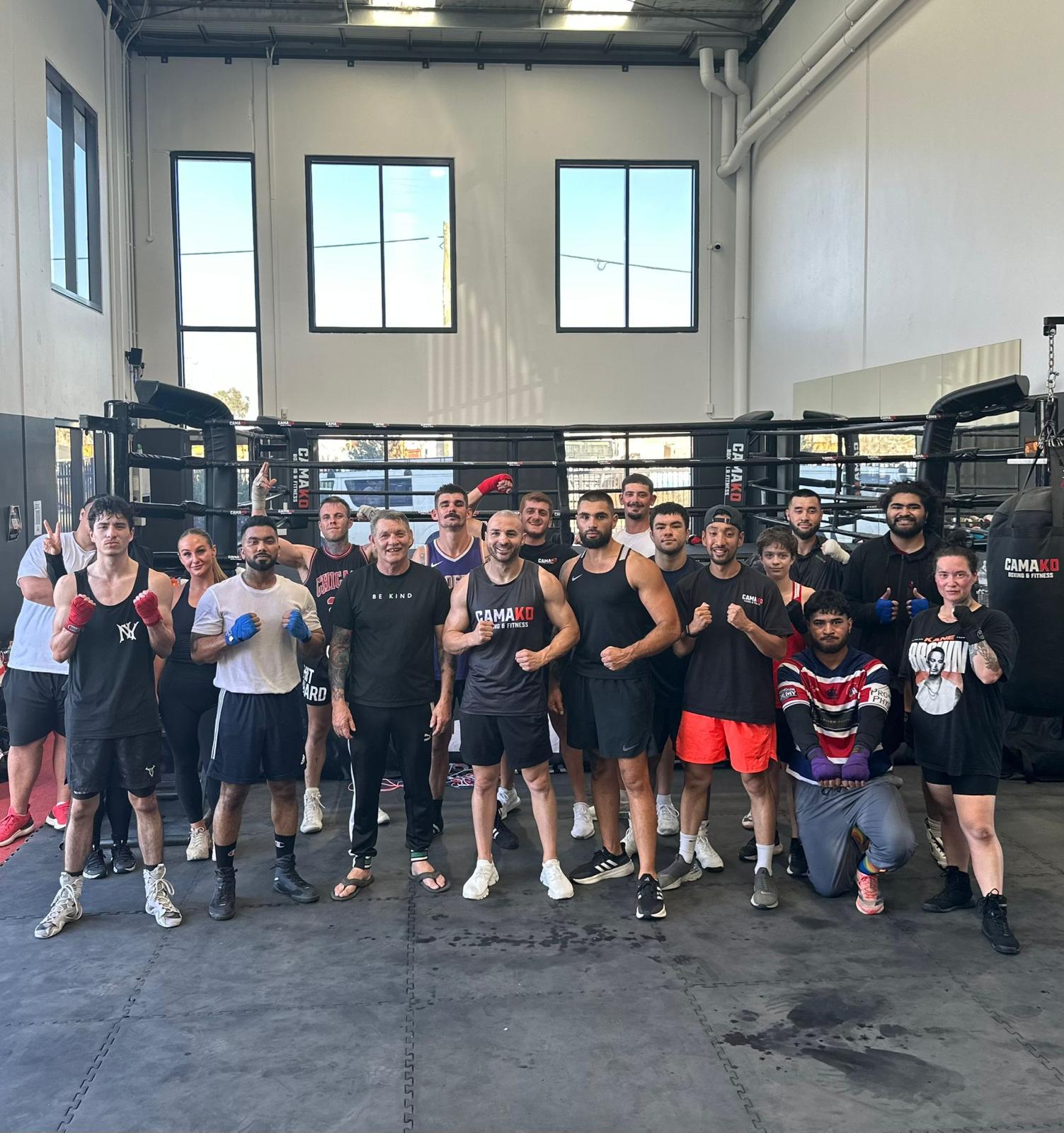 A group of participants and coaches posing together on the floor of the Cama KO gym