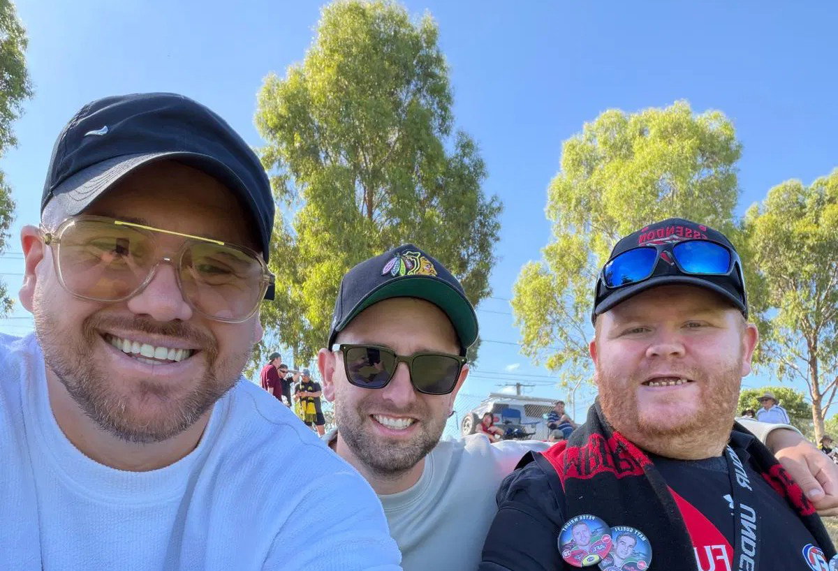 Three men smiling together in a selfie at an outdoor event