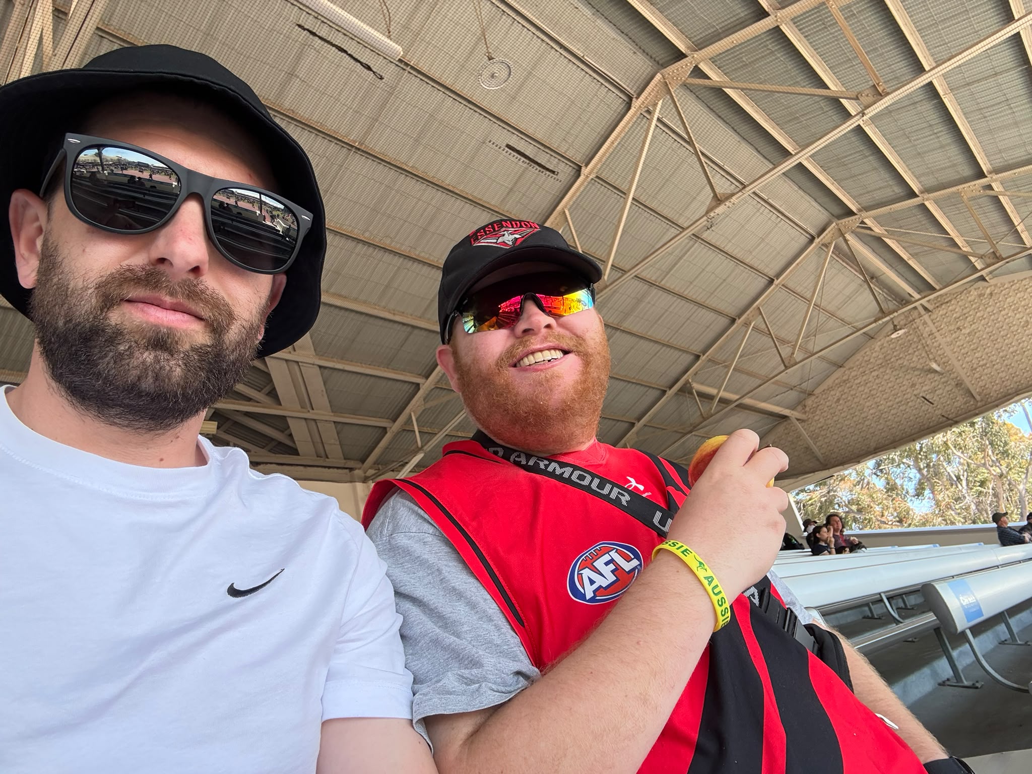A support worker and a participant in an Essendon jumper in a selfie at the footy
